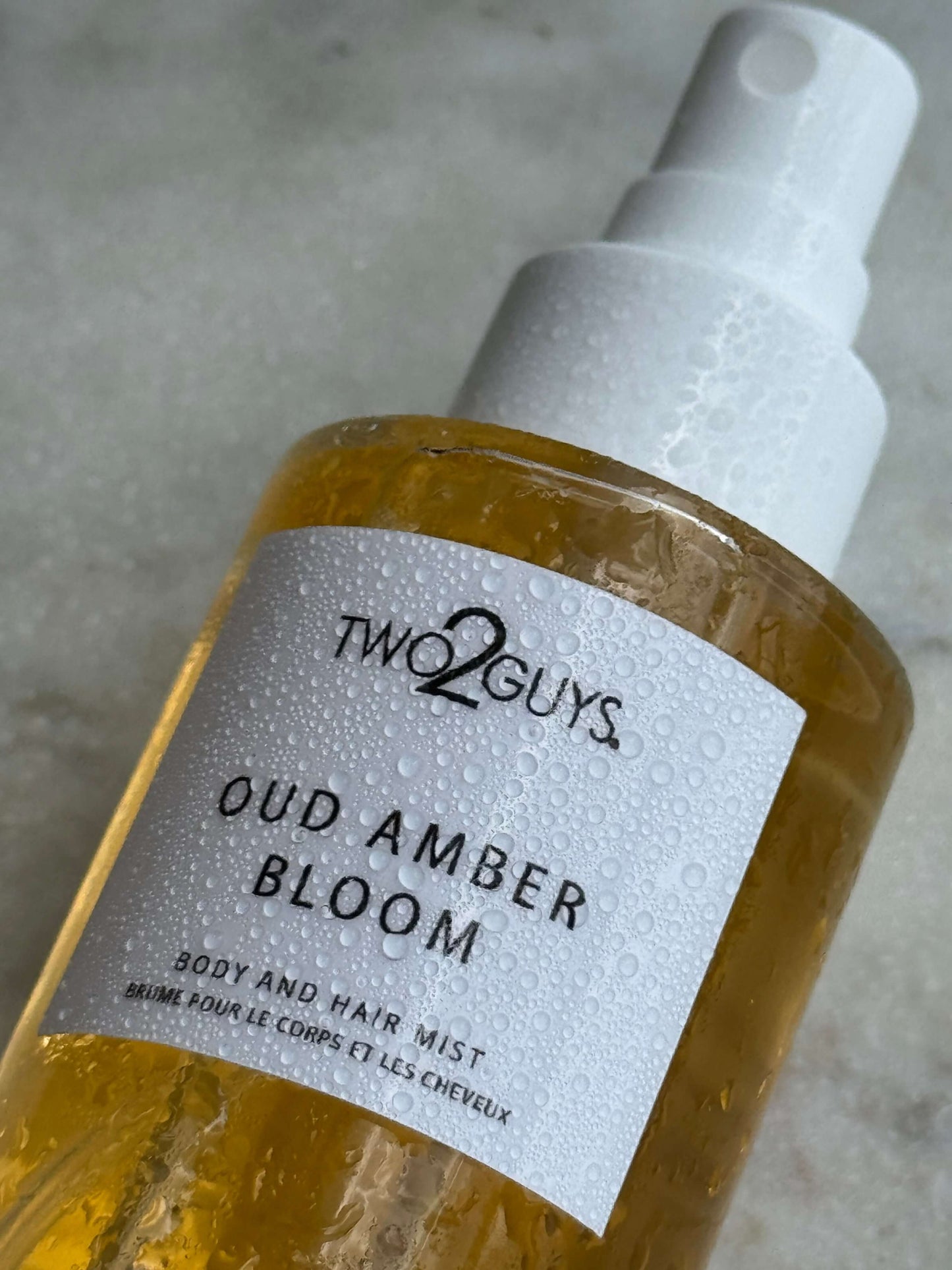 Bottle of Oud Amber Bloom Body and hair mist by TWO2GUYS on a gray surface