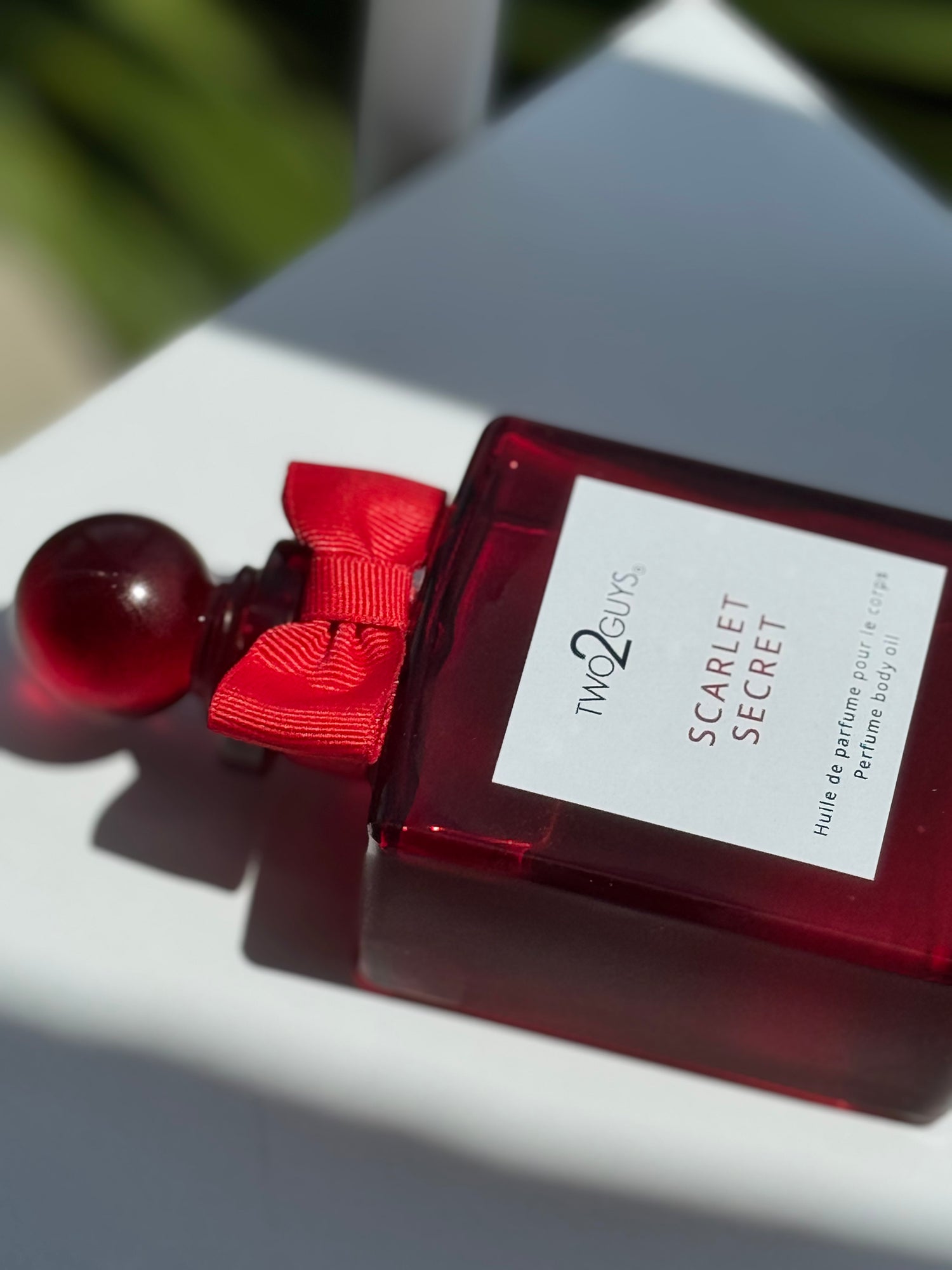 Red perfume bottle with a red bow labeled 'Scarlet Secret' by 'Two Guys' on a white surface.
