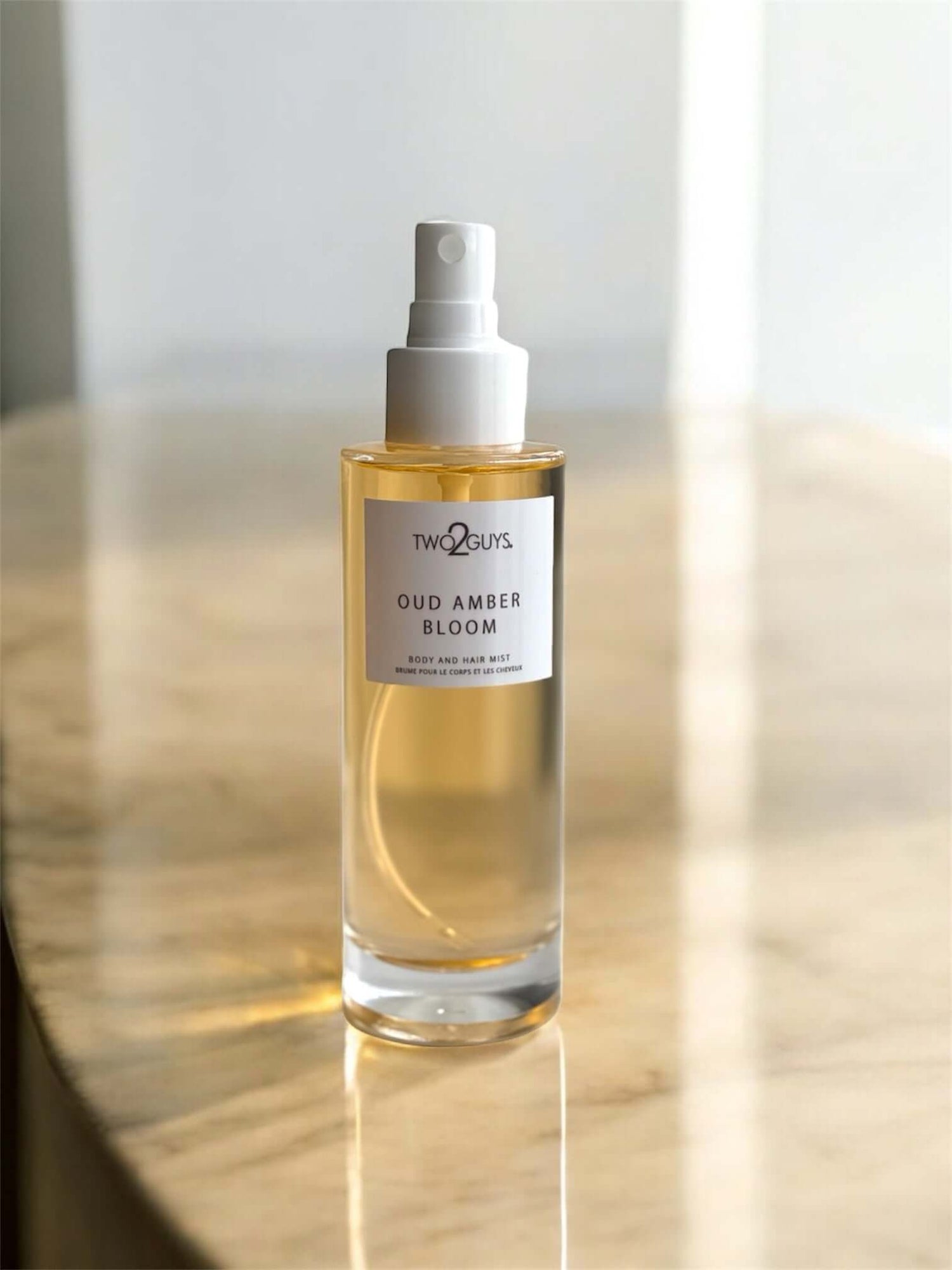 A bottle of Oud Amber Bloom perfume by Two2Guys on a wooden surface with a neutral background with notes of oud, amber and sandalwood