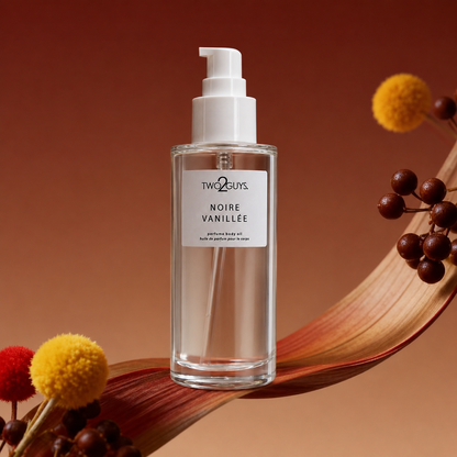 A bottle of Two Guys Noire Vanille body oil with a white pump dispenser, set against a warm brown background with decorative dried leaves and pom-pom flowers.