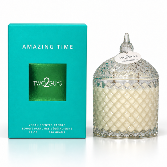 A Two Guys 'Amazing Time' vegan scented candle in a clear diamond-cut glass jar with a lid, shown next to its bright turquoise packaging box on a white background.