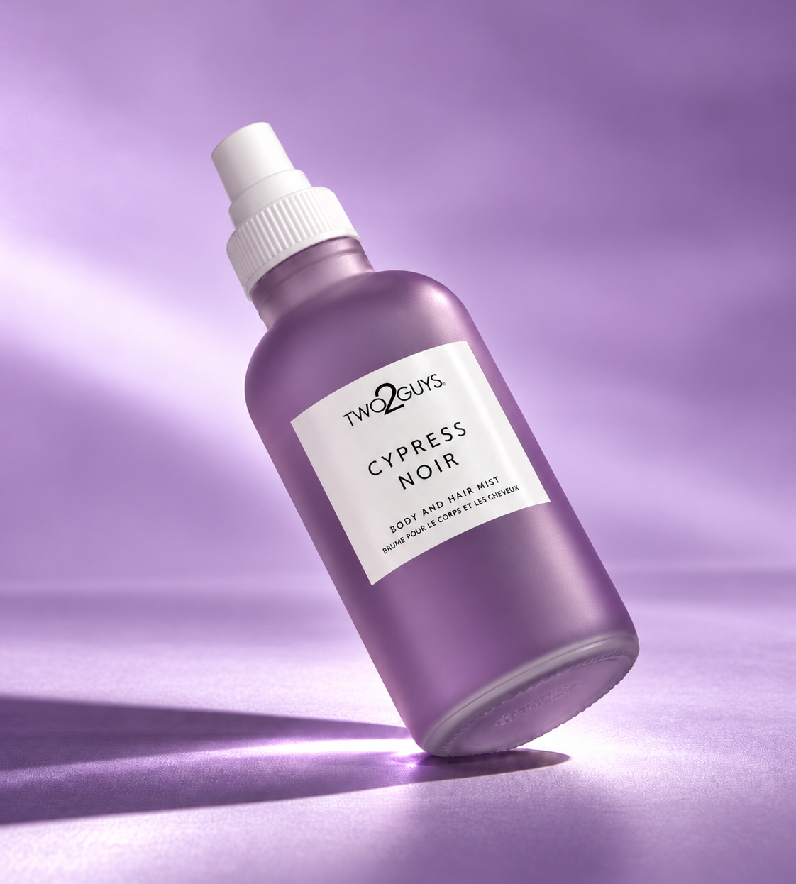 A purple spray bottle of Two2Guys Cypress Noir body and face bath mist, set against a matching purple studio background with a soft spotlight effect.