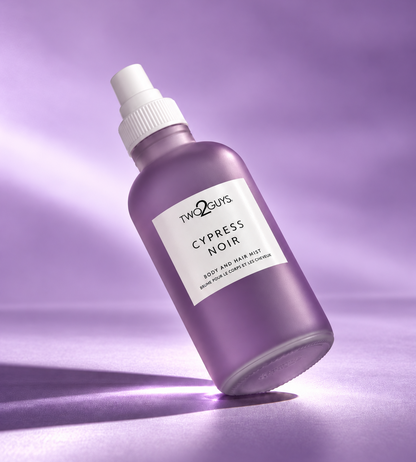 A purple spray bottle of Two2Guys Cypress Noir body and face bath mist, set against a matching purple studio background with a soft spotlight effect.