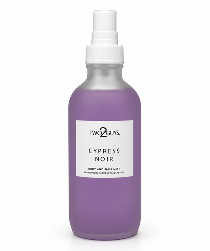 A frosted glass spray bottle filled with lavender-purple liquid, featuring a white spray top and a white rectangular label that reads 'TWO2GUYS. CYPRESS NOIR BODY AND HAIR MIST'.