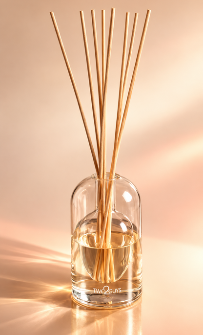 A clear glass reed diffuser bottle with natural bamboo reeds, set against a warm beige background with soft diagonal shadows.