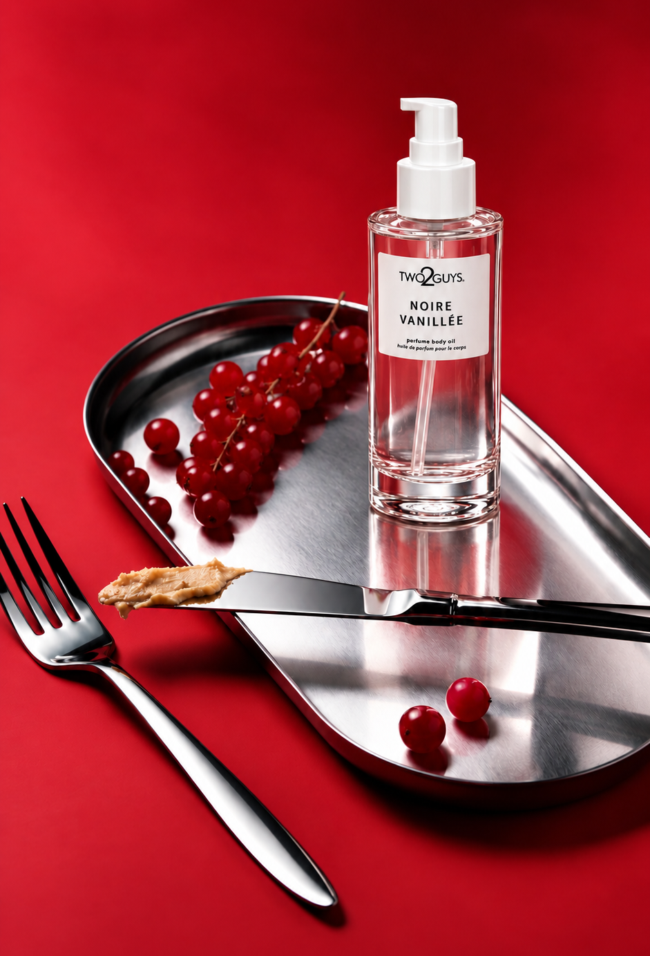 A bottle of Noche de Rose Élixir Noire Vanillee hand sanitizer sits on a silver metal tray with a fork and knife, surrounded by red berries on a solid red background.