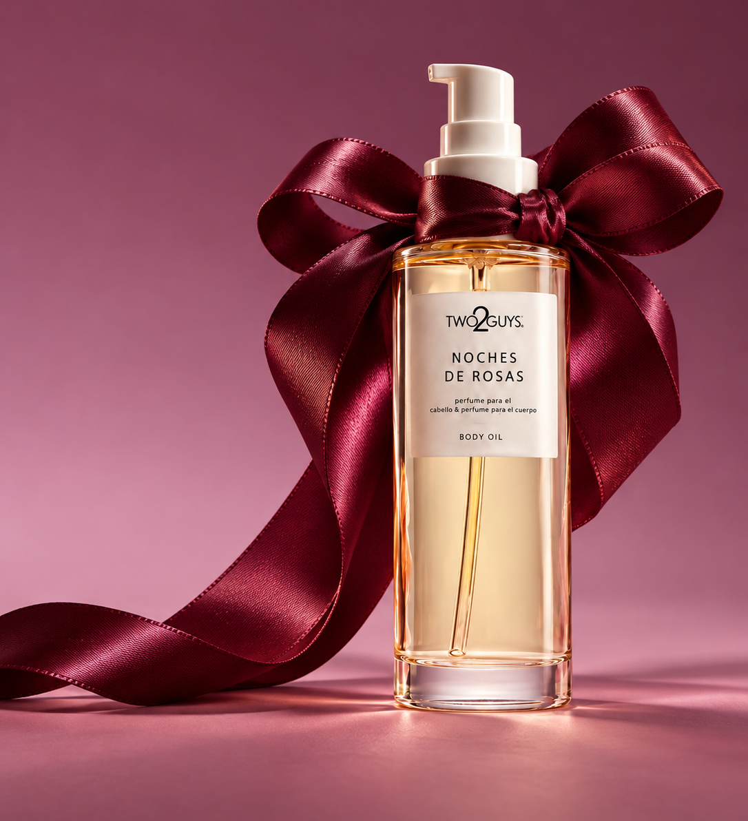 A bottle of Noches de Rosas body oil, decorated with a large dark red satin bow, set against a solid mauve-pink background.