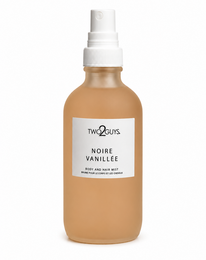 A frosted glass spray bottle of Two2Guys Noire Vanillée body and hair mist, filled with a warm tan liquid, featuring a white label and white spray nozzle on a white background.