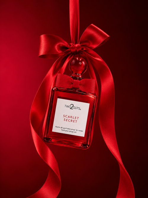 A red perfume bottle labeled 'Two2guys Scarlet Secret' tied with a large red satin ribbon and bow, set against a dark red background.