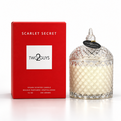 A Two2Guys Scarlet Secret vegan scented candle in a clear cut-glass jar with a pointed lid, shown next to its red product box on a white background.