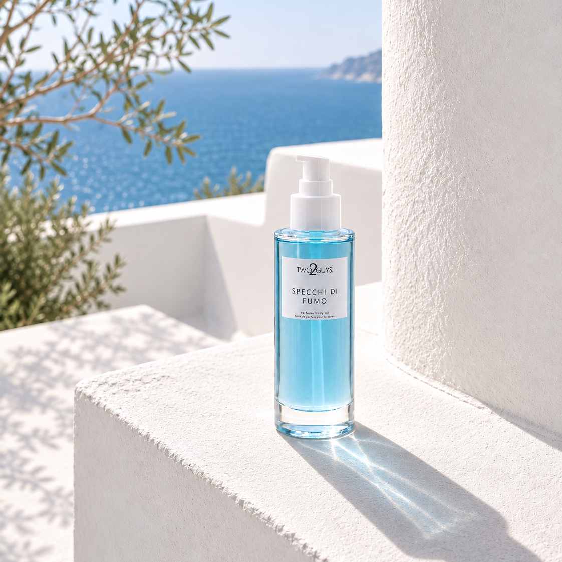 A clear glass spray bottle filled with light blue liquid stands on a white stucco ledge outdoors, with the sea and olive tree branches visible in the background. The bottle label reads 'The 247' and 'SPECIAL FOAM'.