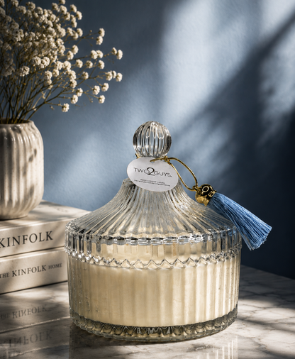 Decorative glass jar with a tassel on a marble surface with books and flowers in the background.